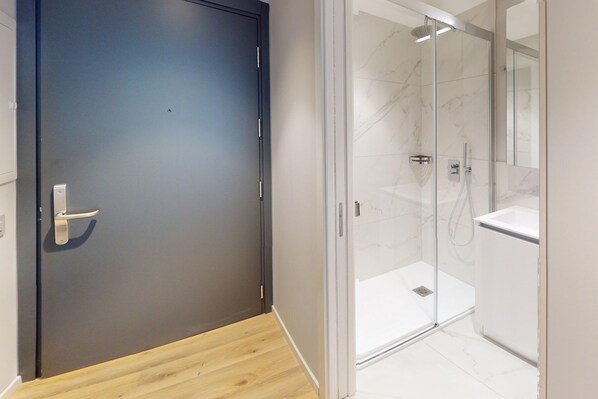 Un baño moderno con cabina de ducha de vidrio, un lavabo blanco y una puerta oscura.