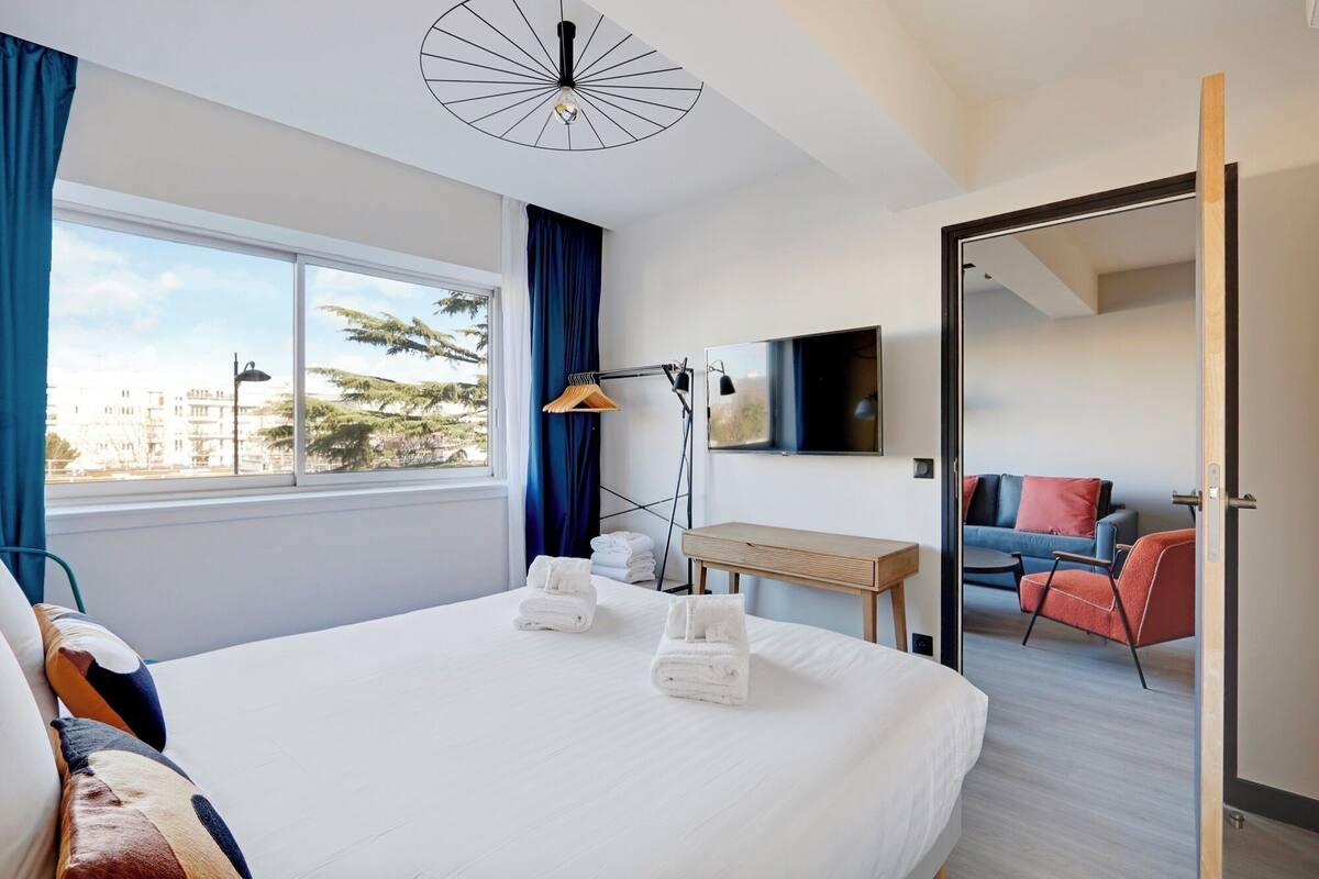 Habitación de hotel con una cama grande, un escritorio, una silla, un televisor y vistas a la ciudad.