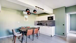 Una cocina moderna con armarios blancos, un microondas y un lavabo. Hay una zona de comedor con una mesa y sillas de madera.