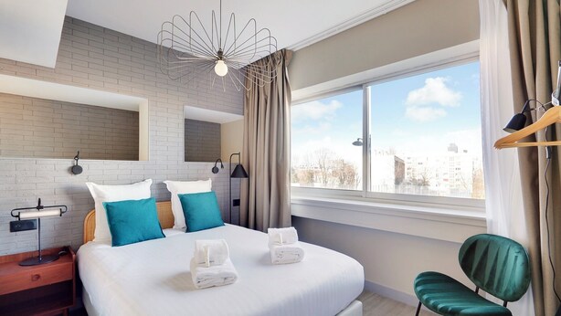 Habitación de hotel moderna con una cama grande, vistas a la ciudad y una silla verde.