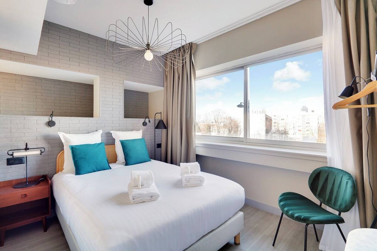 Habitación de hotel moderna con una cama grande, vistas a la ciudad y una silla verde.