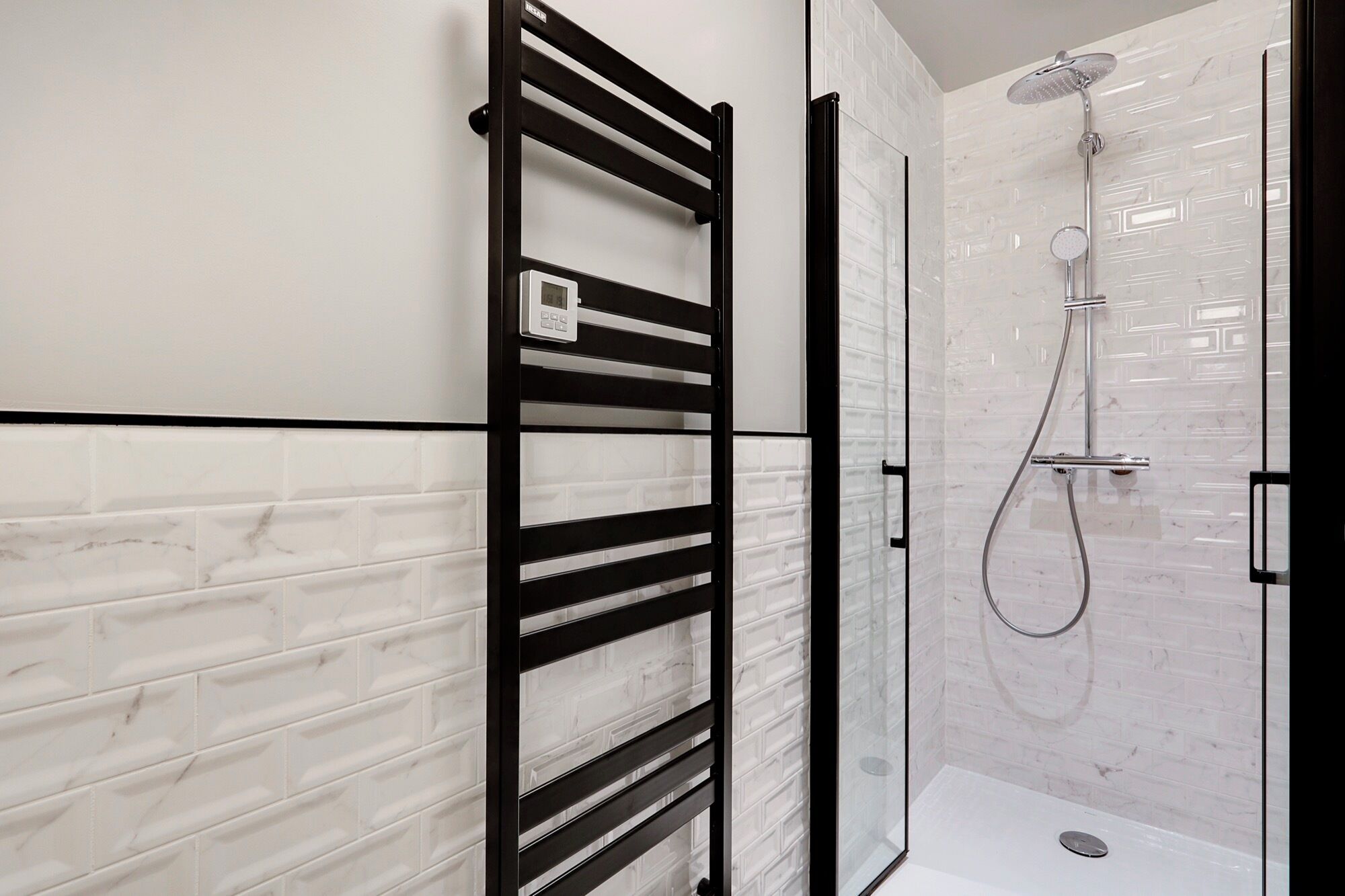 A modern bathroom with a glass shower enclosure, a black towel rack, and white marble tiles.