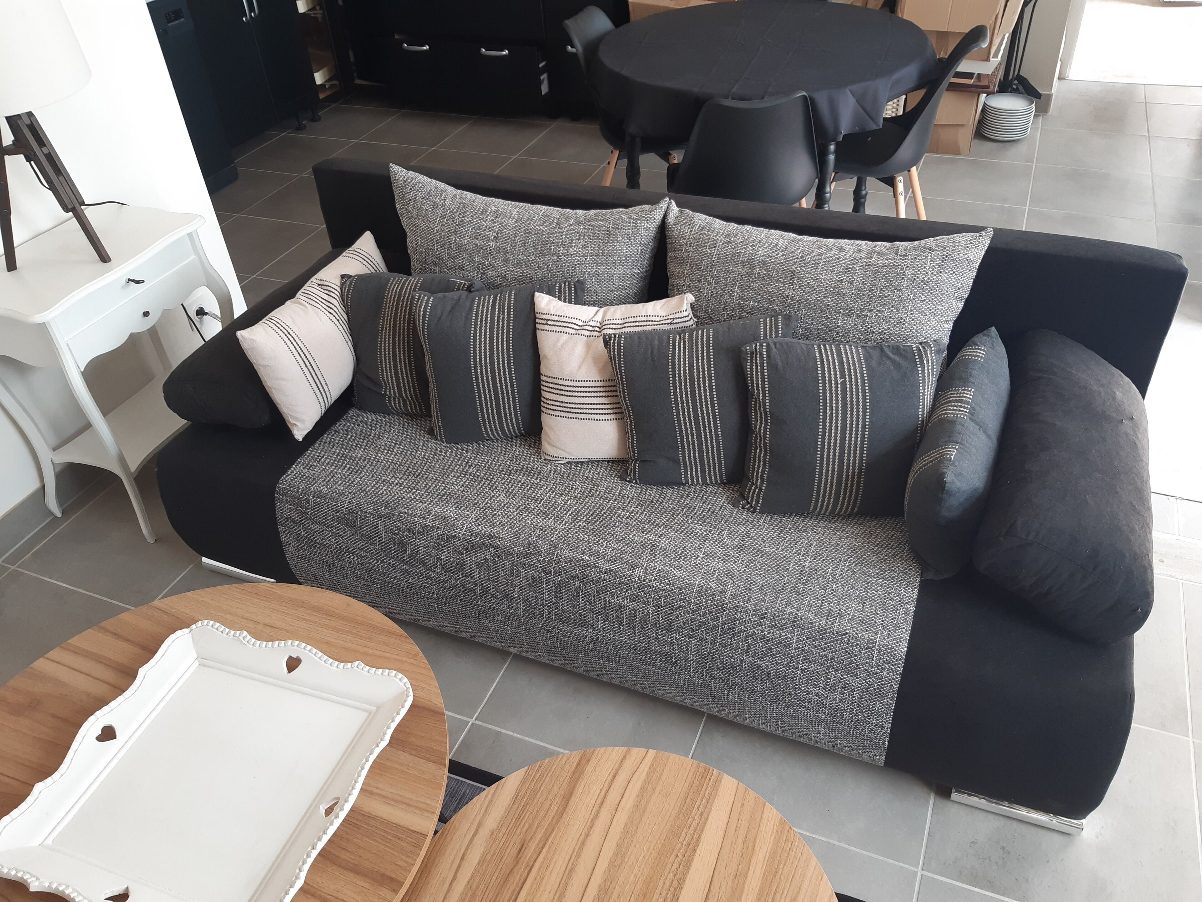Una sala de estar moderna con un sofá de color gris oscuro y estampado, varios cojines, una mesita de noche blanca y una mesa de centro de madera.