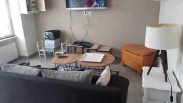 Een woonkamer met een aan de muur bevestigde televisie, een bank, een salontafel, een lamp en een klein houten kastje.