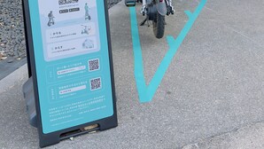 Monopattini elettrici parcheggiati di fronte a un edificio con un cartello che mostra istruzioni e codici QR.