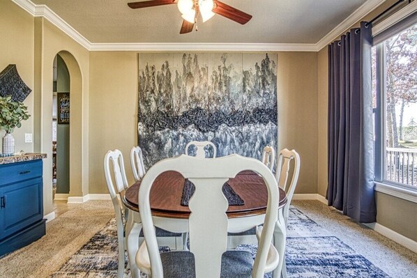 A dining area with a round table, white chairs, a blue cabinet, and a large abstract painting on the wall.