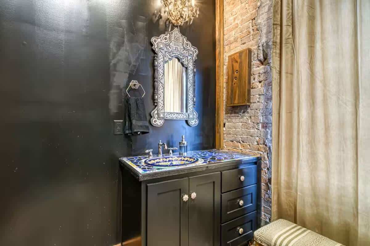 A bathroom with a black vanity, a mirror with a decorative frame, and a sink with a blue and white patterned countertop.