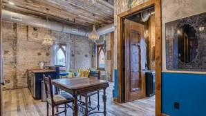 Una zona de menjador rústica amb taula i cadires de fusta, un penjallum i una paret de pedra.
