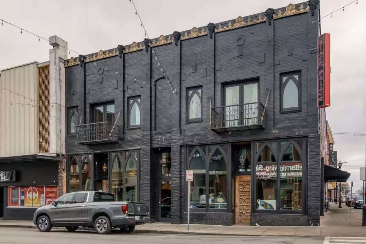 A two-story building with a dark facade, large windows, and a balcony on the second floor.