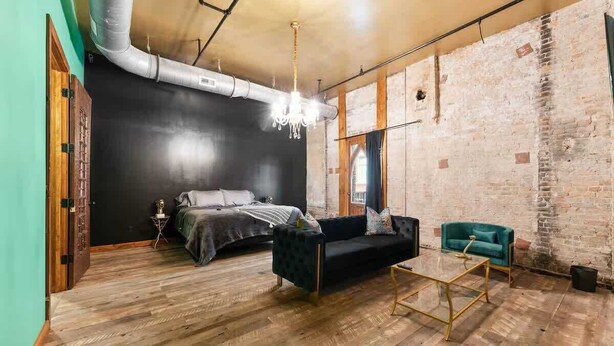A room with a bed, a dark sofa, a teal armchair, a glass coffee table, and exposed brick walls. - Welcome to Black Palace-D! A beautiful downtown loft with easy access to everyth (Springfield)