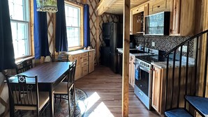 Et rummeligt køkken med træskabe, et spiseområde med bord og stole, og en trappe til en etage ovenpå.