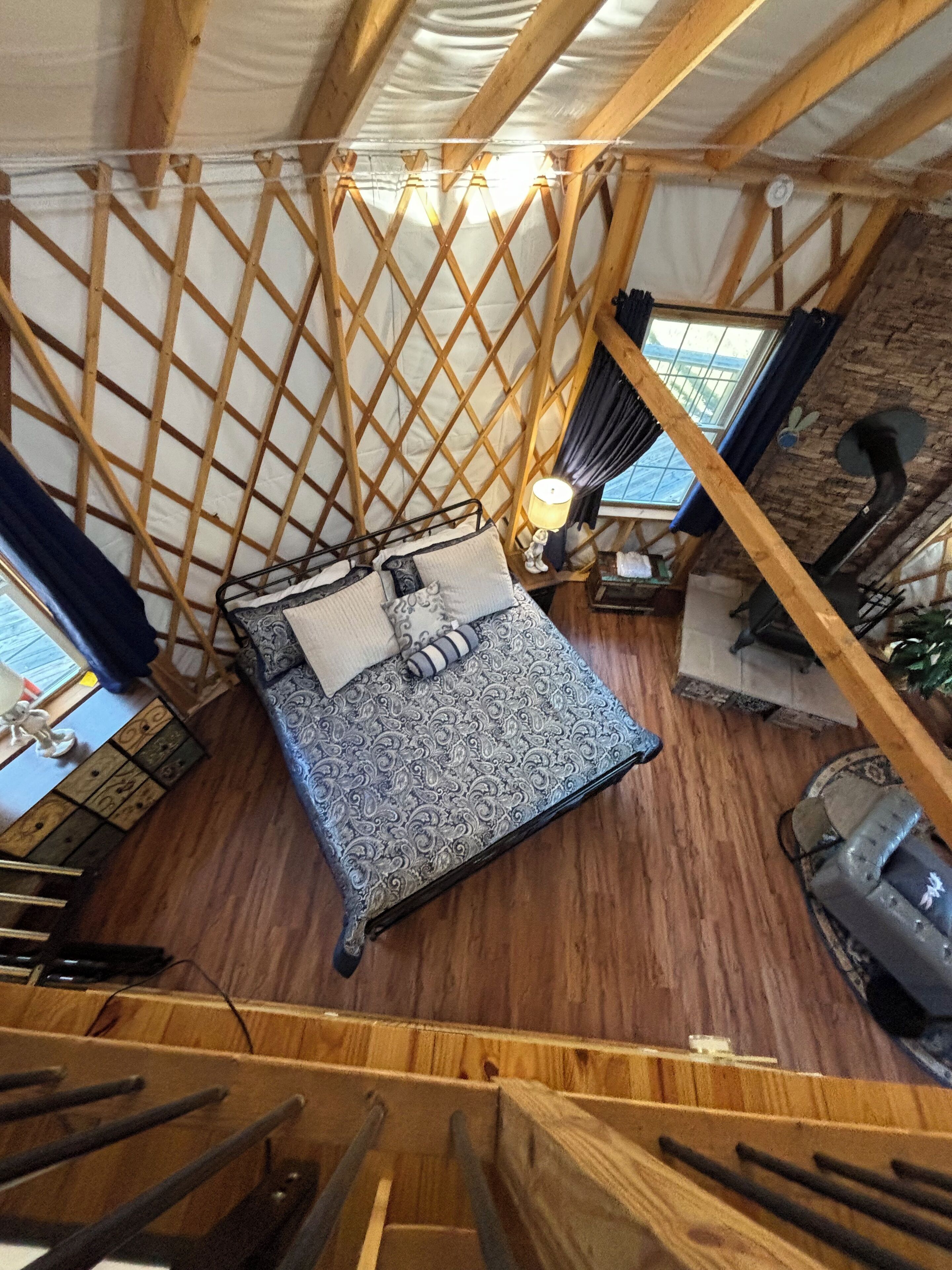 Une pièce aux hauts plafonds, dotée d’un plancher en bois, d’un lit avec une literie à motifs, d’une lampe et d’une cheminée rustique.