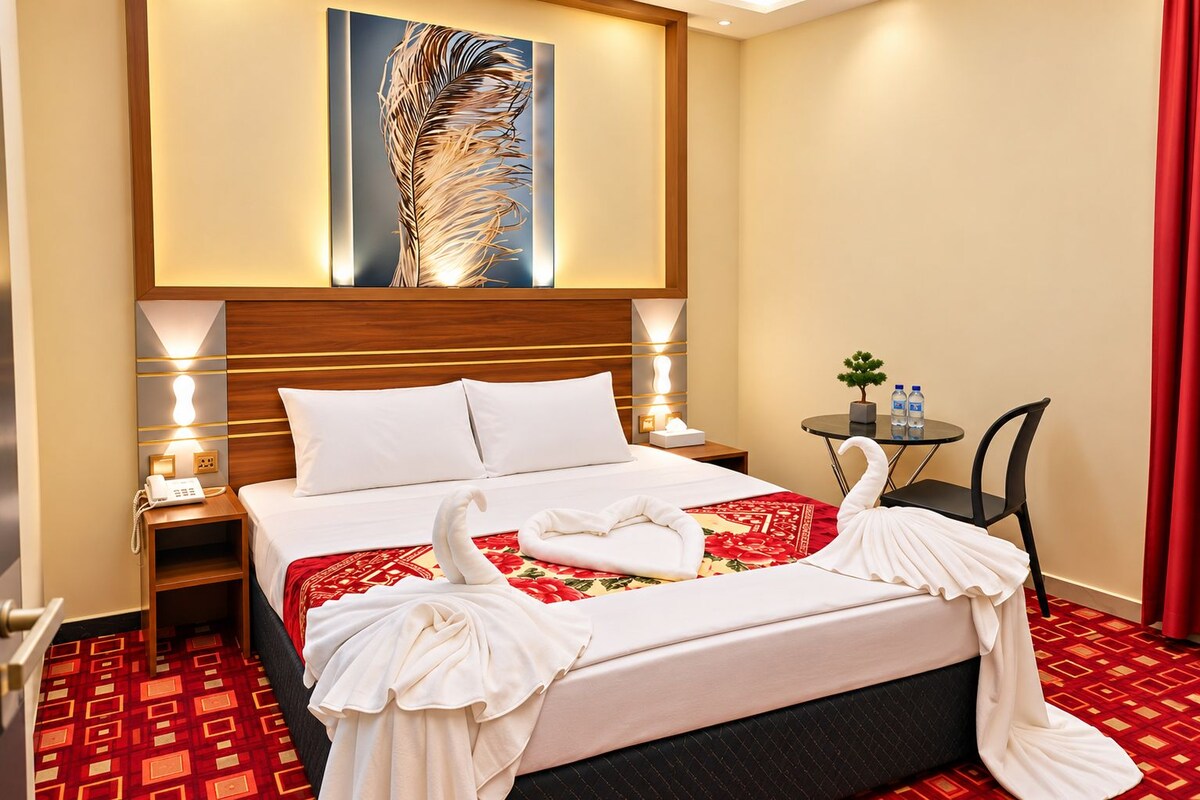 A hotel room with a bed, bedside lamps, a small table with water bottles, and a decorative wall piece.