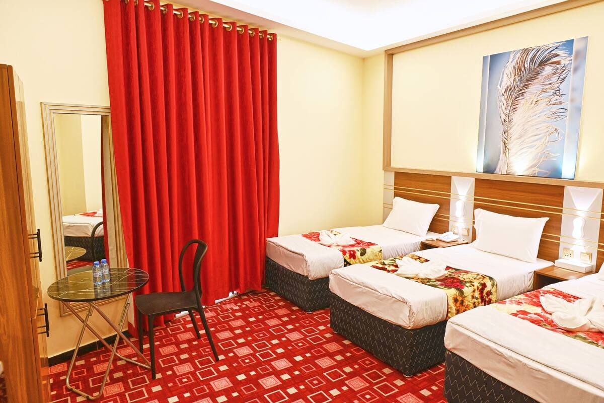 A hotel room with two beds, a small table with chairs, a mirror, and a red curtain.