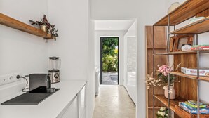 Eine moderne Küche mit Arbeitsplatte, Mixer und Kaffeemaschine. Ein Holzregal zeigt eine Blumenvase und eine Taschentuchbox.
