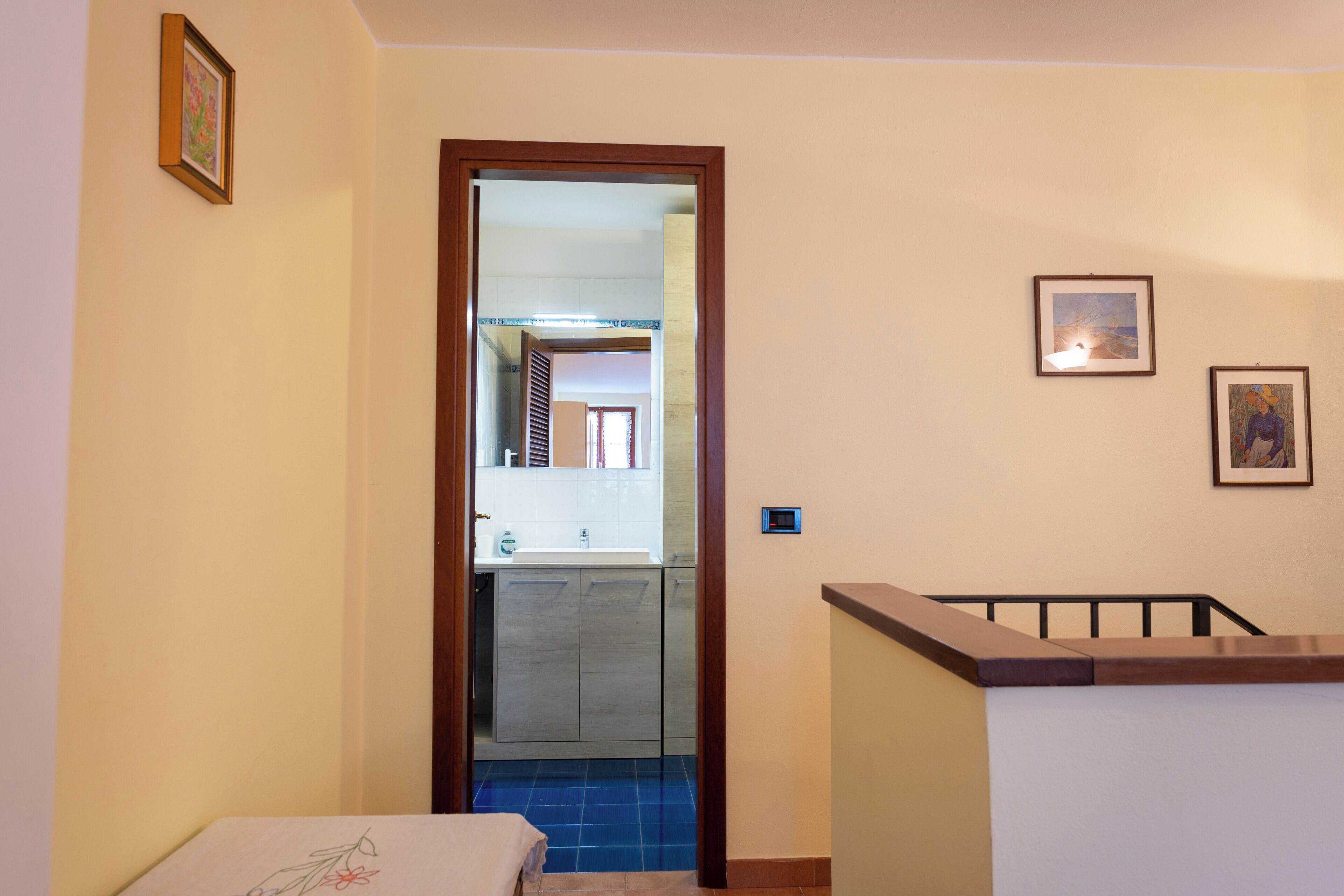 A narrow hallway with a wooden door leading to a kitchen area. There are two framed pictures on the wall.