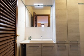 Et badeværelse med en hvid vask, et spejl og træskabe.