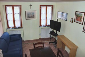 A room with a blue sofa, a wooden table, a television, and two windows with curtains.