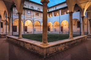 A courtyard with arches and columns, a grassy area, and a building with multiple windows.