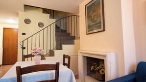 A dining area with a table set for two, a vase of flowers, a fireplace with sunflowers, a staircase, and a painting on the wall. - Suite Carla Cozy Apartment in Petrasanta Center (Pietrasanta)