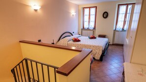A bedroom with a bed, two wall-mounted lights, a window with curtains, a radiator, and a wooden staircase railing. - Suite Carla Cozy Apartment in Petrasanta Center (Pietrasanta)