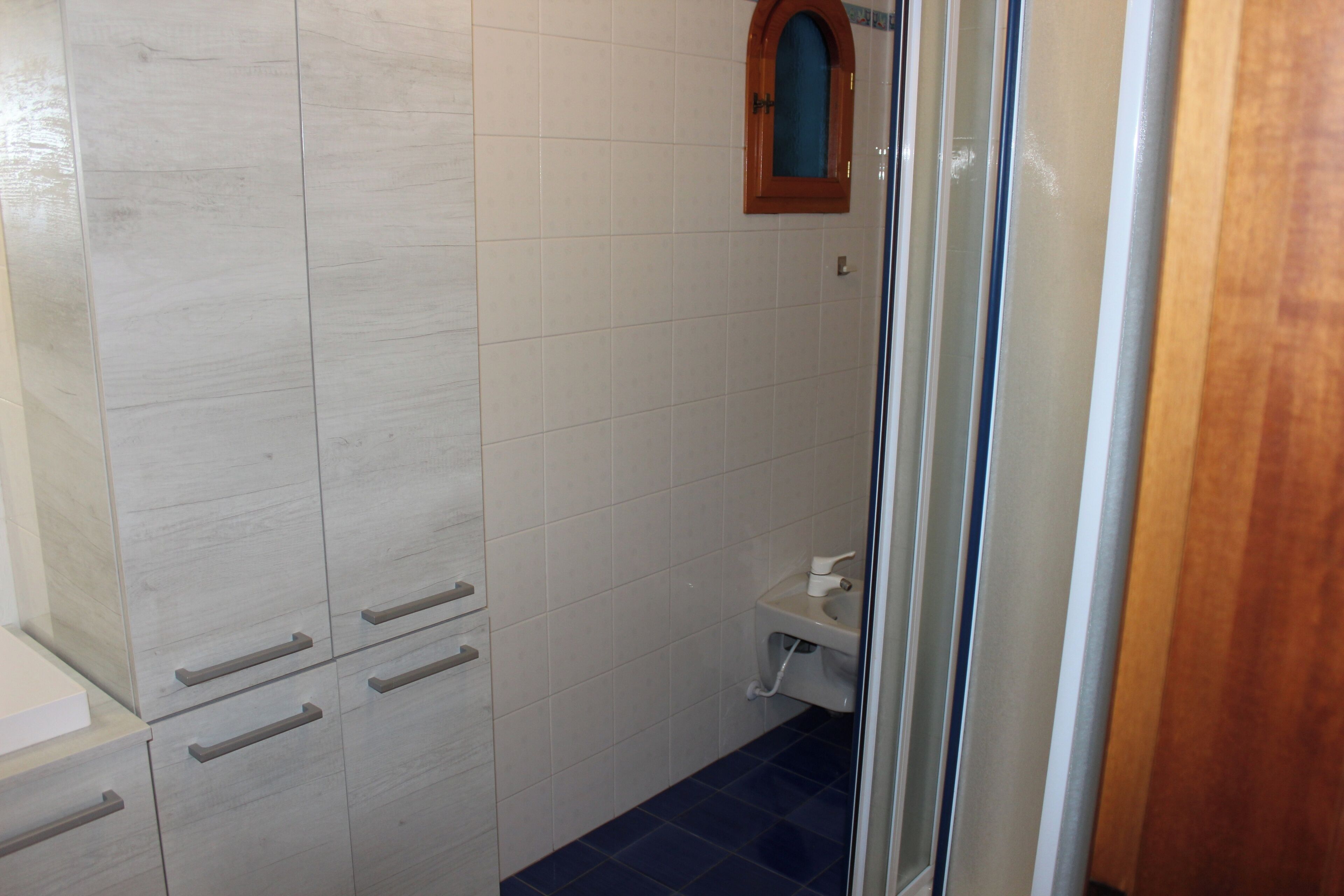 A bathroom with white tiled walls, a wooden-framed mirror, a white sink, and a blue-tiled floor.