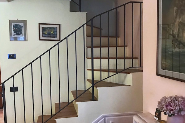 A staircase with a black metal railing, wooden steps, and two framed artworks on the wall. - Suite Carla Cozy Apartment in Petrasanta Center (Pietrasanta)