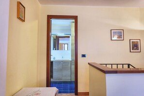 A hallway with a wooden railing, a tiled floor, and a door leading to a bathroom with a sink and mirror. - Suite Carla Cozy Apartment in Petrasanta Center (Pietrasanta)