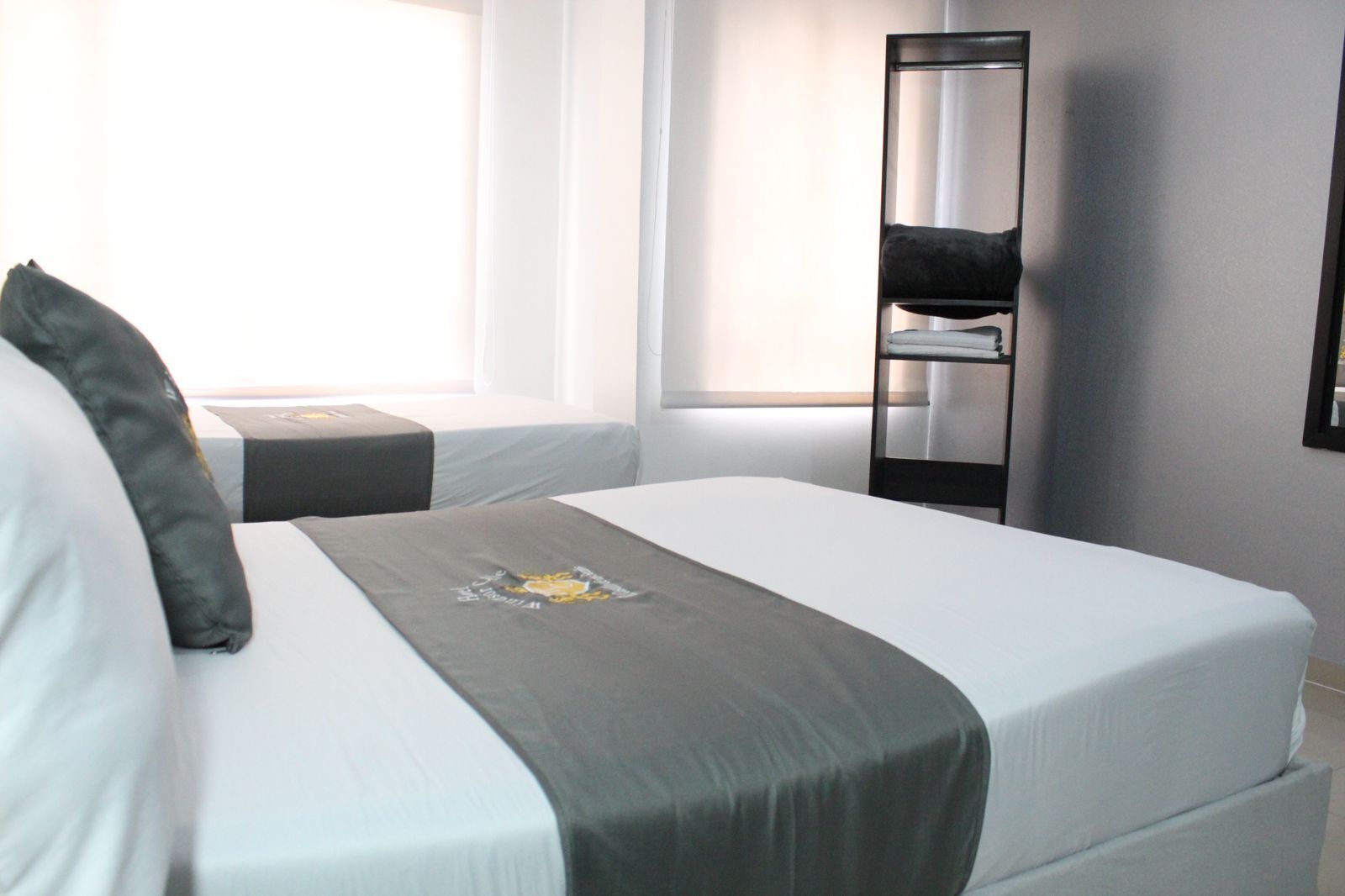 A hotel room with two single beds, a bedside table, a chair, and a tall mirror on the wall.