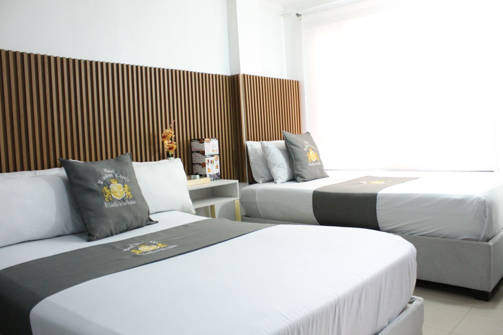 A hotel room with two beds, a wooden headboard, a small table with a vase, and a window with a view.
