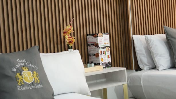 A hotel room with a bed, a nightstand, and a menu board. - Hotel Windsor Colombia (Bogotá)