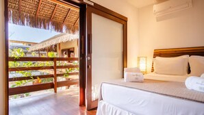 Ein Hotelzimmer mit Bett, Holzboden, einem Strohdach im Freien und Blick auf Grün.