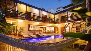 Eine moderne Villa mit Swimmingpool, Sitzgelegenheiten im Freien und einem Balkon mit Reetdach.