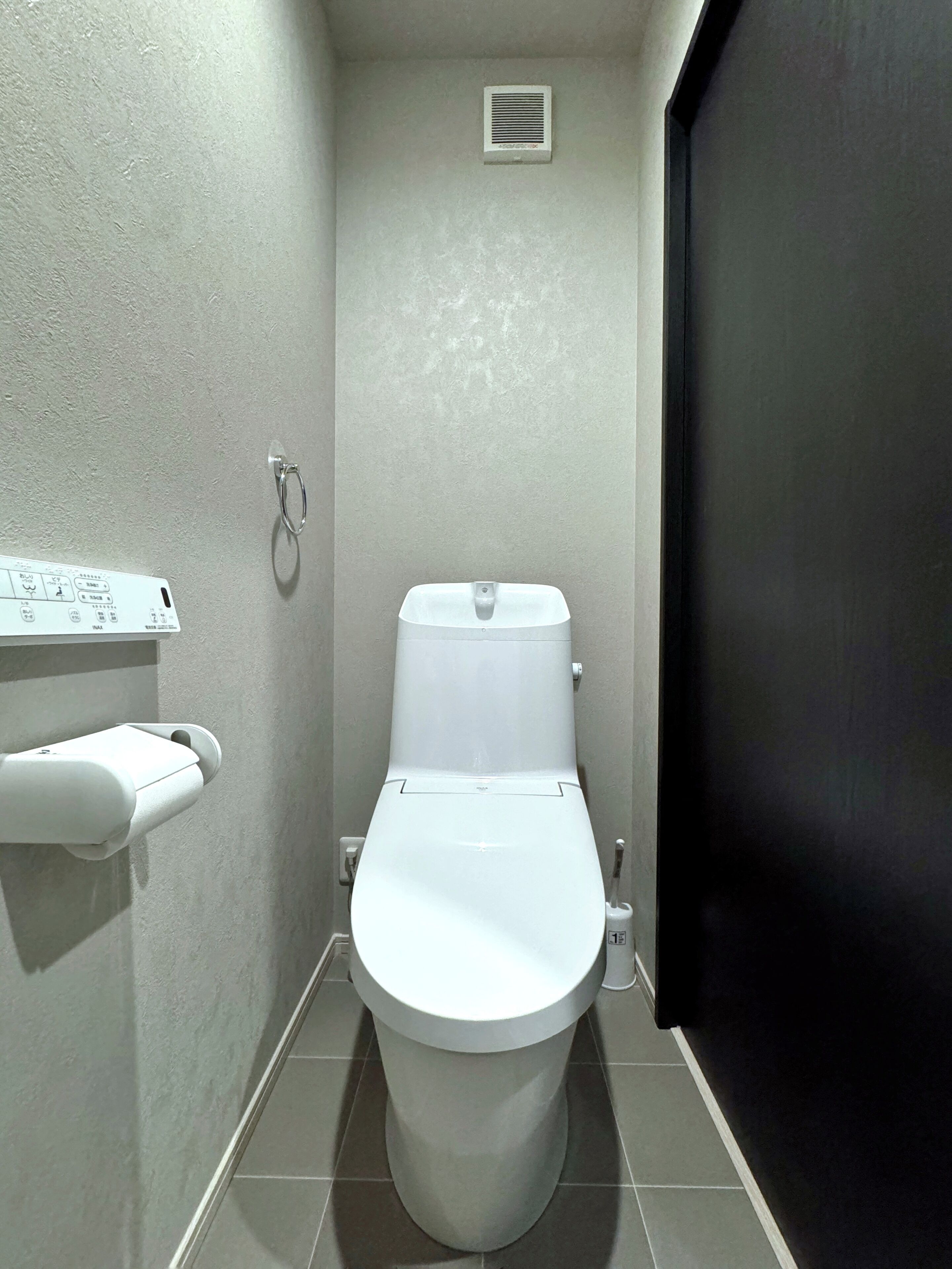 Ein kleines, modernes Badezimmer mit Toilette, Toilettenpapierhalter und Wandlüfter.