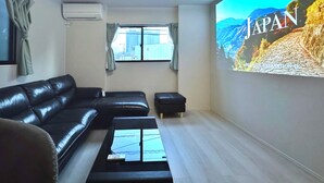A modern living room with a black leather sofa, a coffee table, and a large wall-mounted TV displaying 'JAPAN'. - NEW! [Built in 2024, Entire Newly Built House for Rent / Free Parking Available] Experience Osaka’s Old Town! Conveniently located just 8 minutes by train from Namba! Excellent access to Osaka, Kyoto, and Nara! (大阪市)