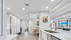 A modern kitchen with white cabinetry, a central island with a sink, and a dining area with a table and chairs.