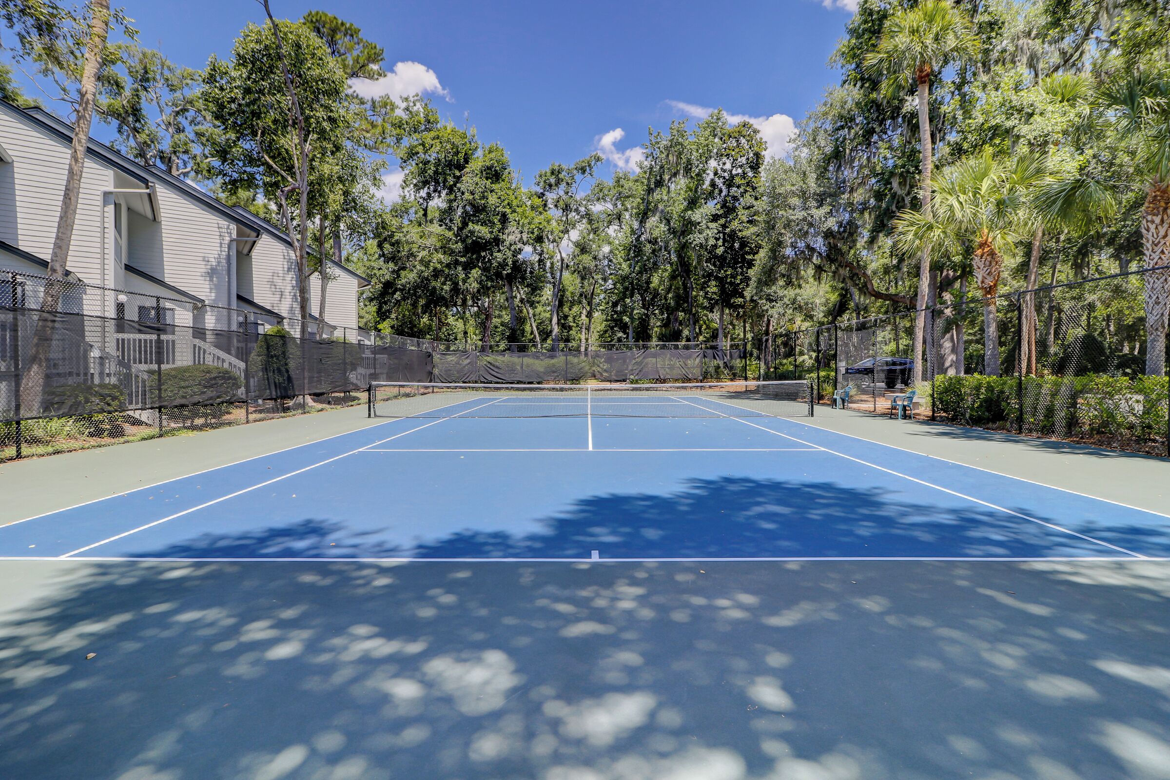 An outdoor tennis court with a net, surrounded by trees and a building.