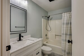Ein Badezimmer mit weißem Waschbecken, Spiegel, Toilette und Badewanne.