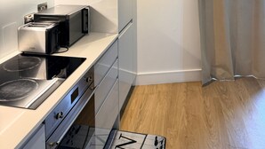 A modern kitchen with a Bosch toaster, a microwave, and a stove. There is a framed artwork on the wall and a wooden floor. - Cozy 2-bed Apt, Sleeps 4 Near Jewellery Quarter (Birmingham)