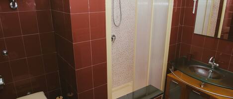Un baño con inodoro, lavamanos de cristal y cabina de ducha.