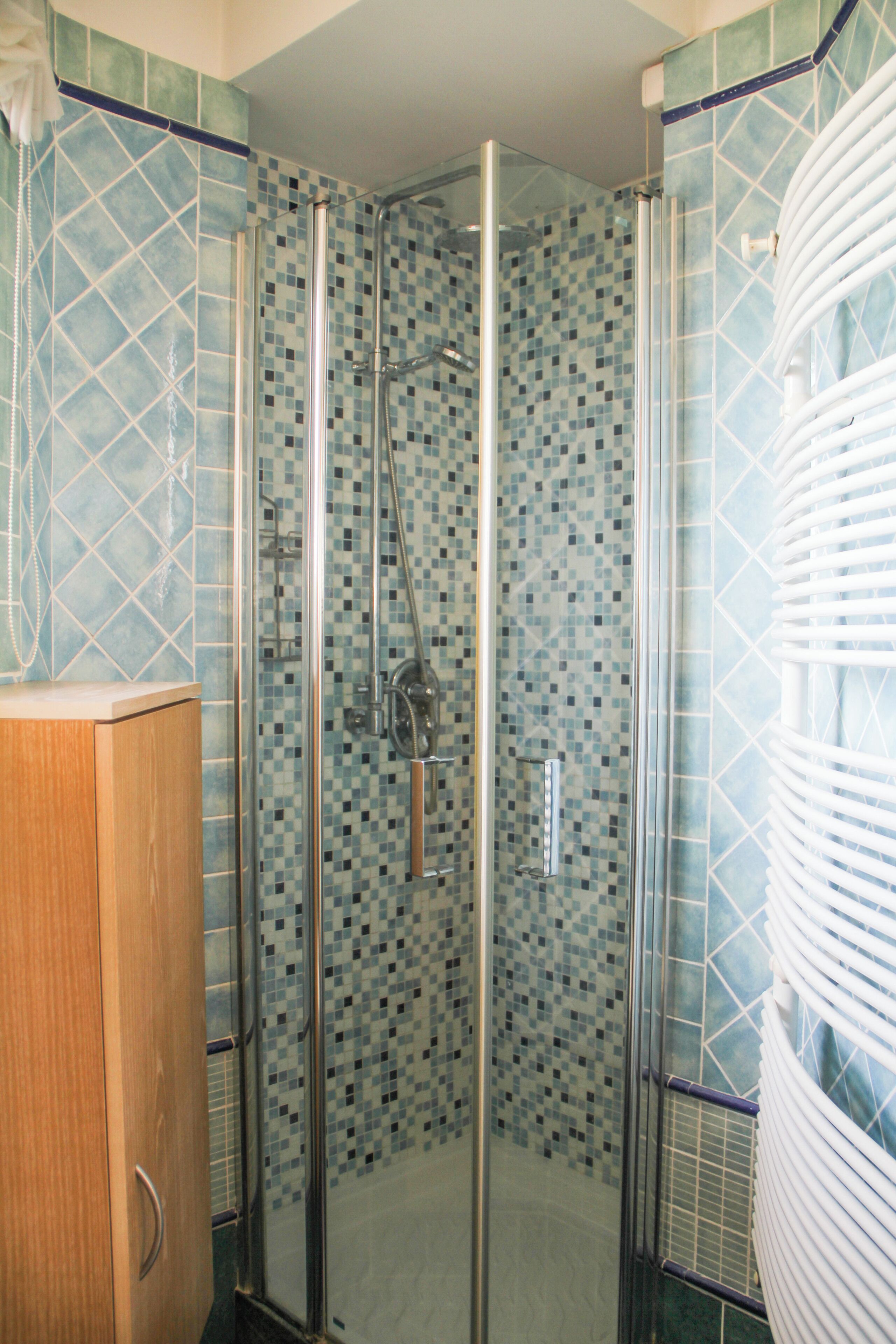 Eine gläserne Dusche mit mosaikverkleideter Wand, einem Holzschrank und einem weißen Handtuchhalter.