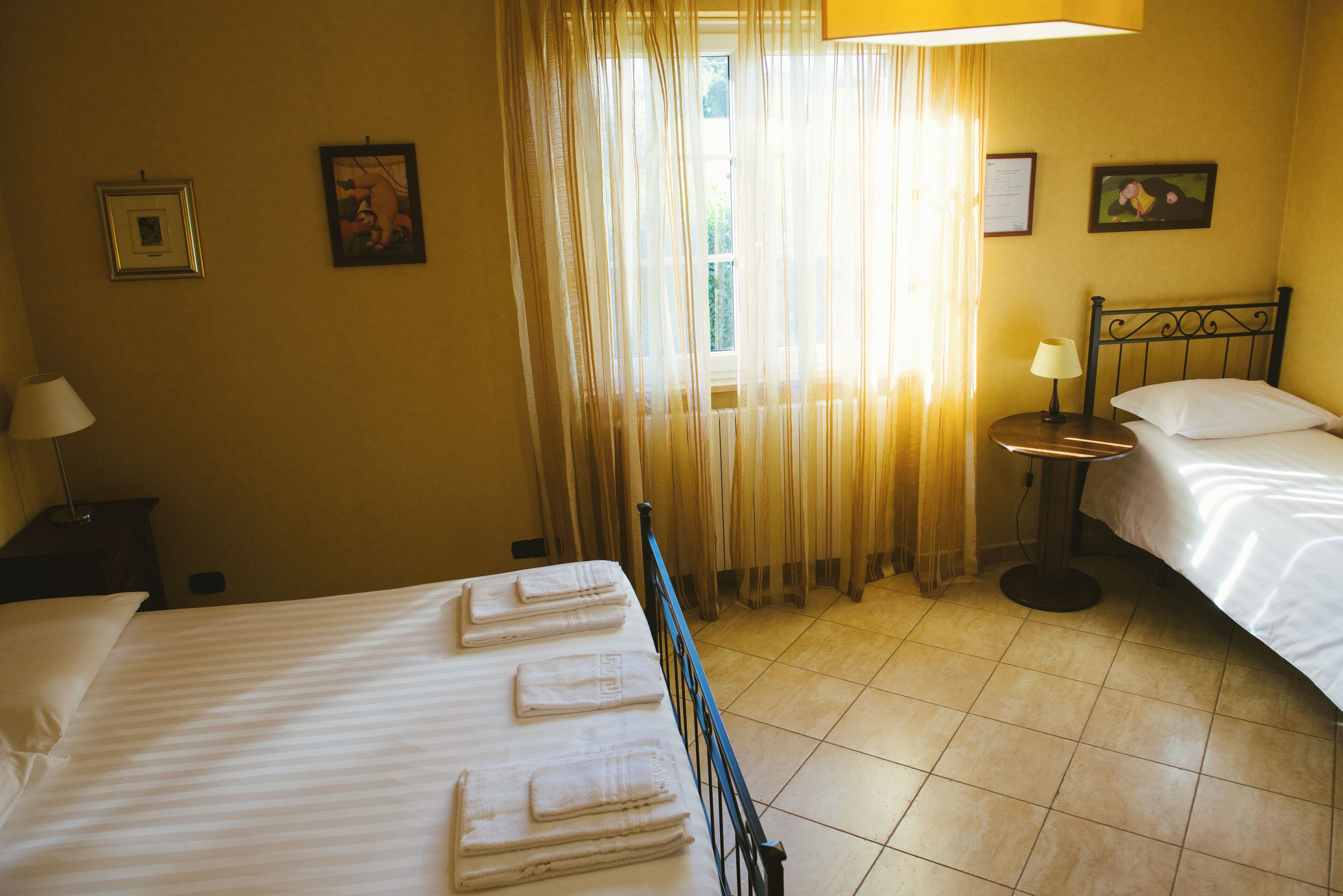 Habitación de hotel con dos camas, una mesita de noche, una lámpara y un ventanal con cortinas.