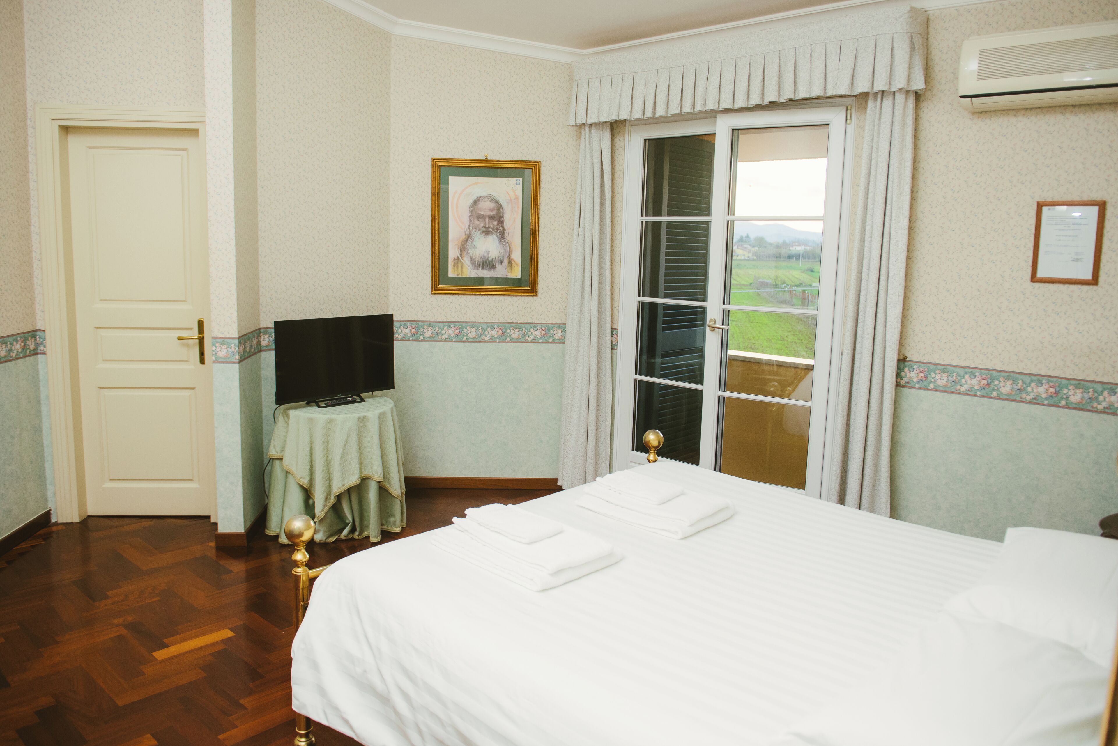 A hotel room with a bed, a television on a small table, a door, and a window with curtains.
