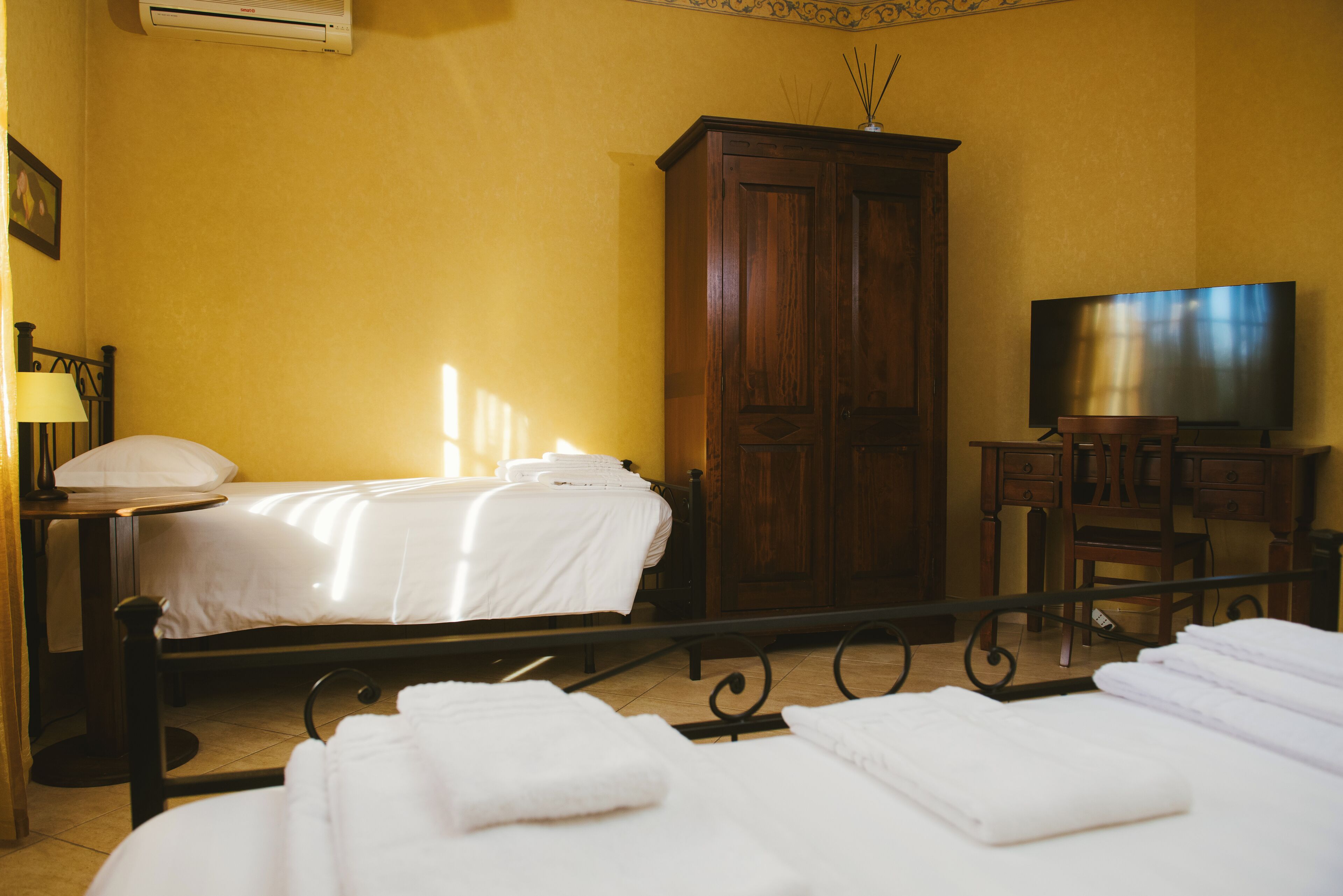 A hotel room with a bed, a wooden wardrobe, a TV, and a desk with drawers.