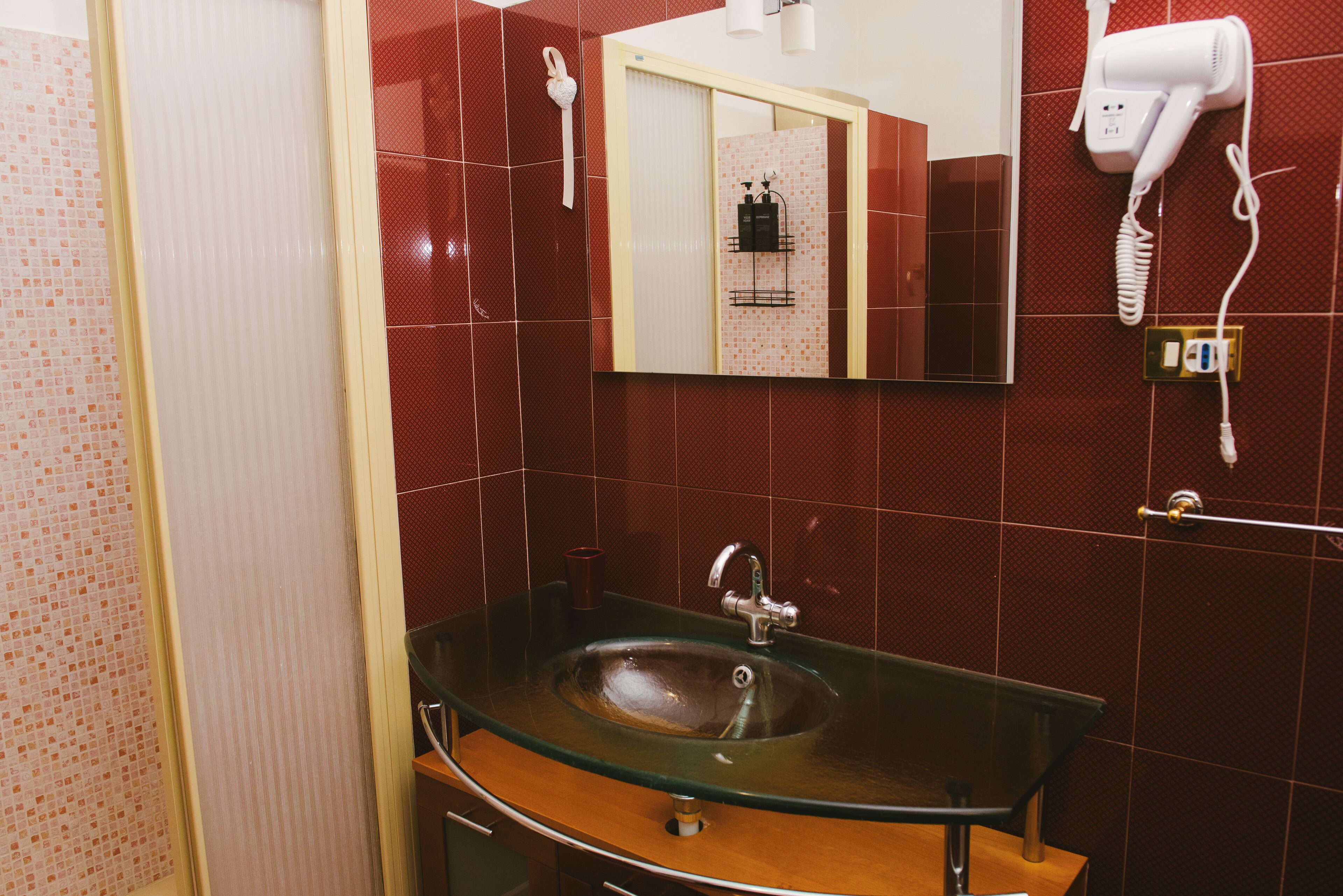 A bathroom with a glass sink, a mirror, a hairdryer, and a towel rack.