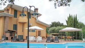 A swimming pool with lounge chairs and umbrellas, a covered patio area, and a building with a yellow facade. - Boteroom Relais (Piedimonte San Germano)