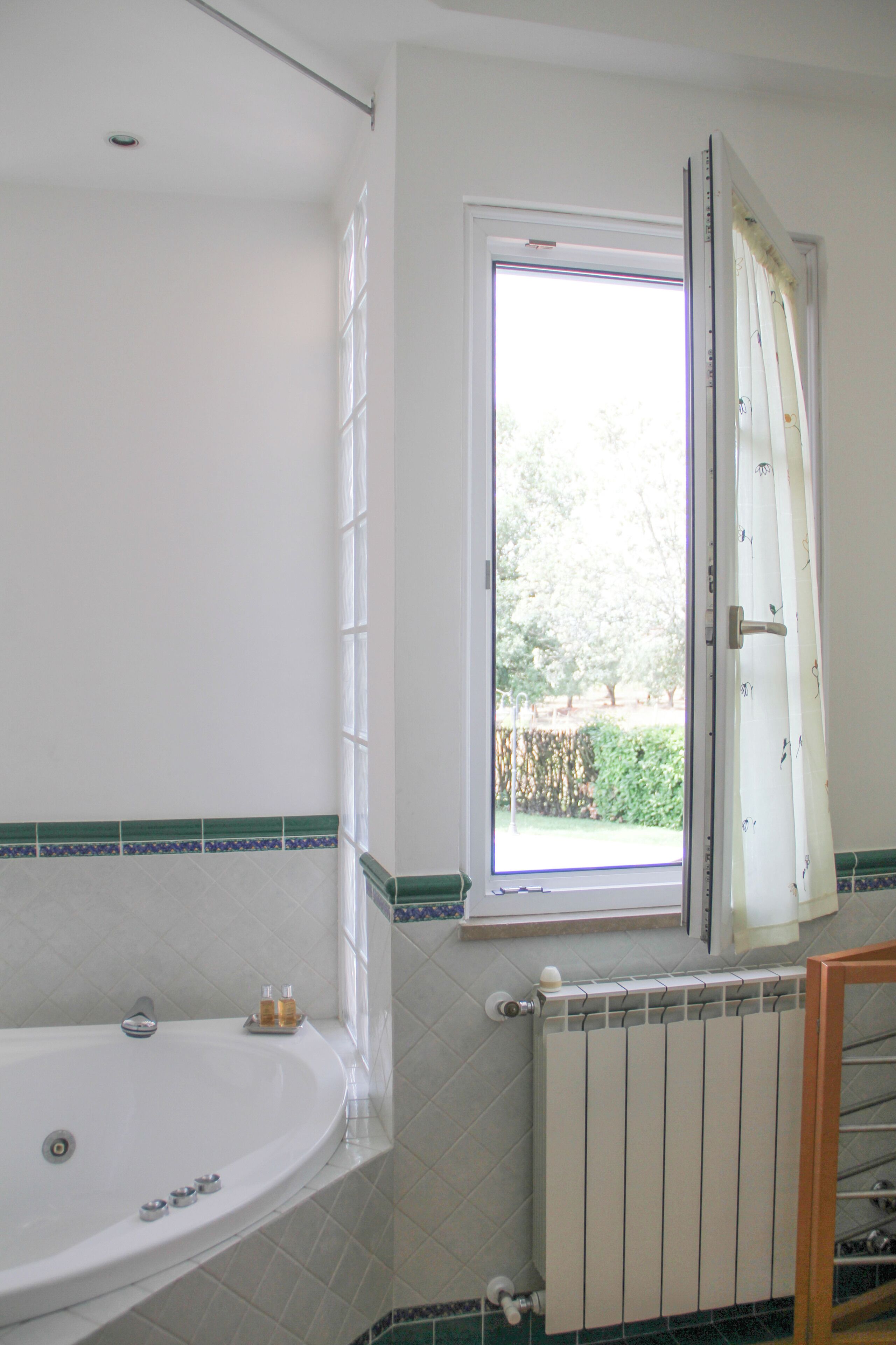 Une salle de bain avec une baignoire, une fenêtre avec des rideaux et un radiateur.