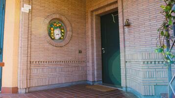 Entrada de un edificio de ladrillo con un elemento decorativo circular en la pared, una puerta verde y una pequeña campana encima.
