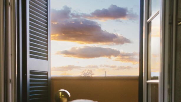 A room with a bed, a window with a view of a sunset, and a door with a window blind. - Boteroom Relais (Piedimonte San Germano)