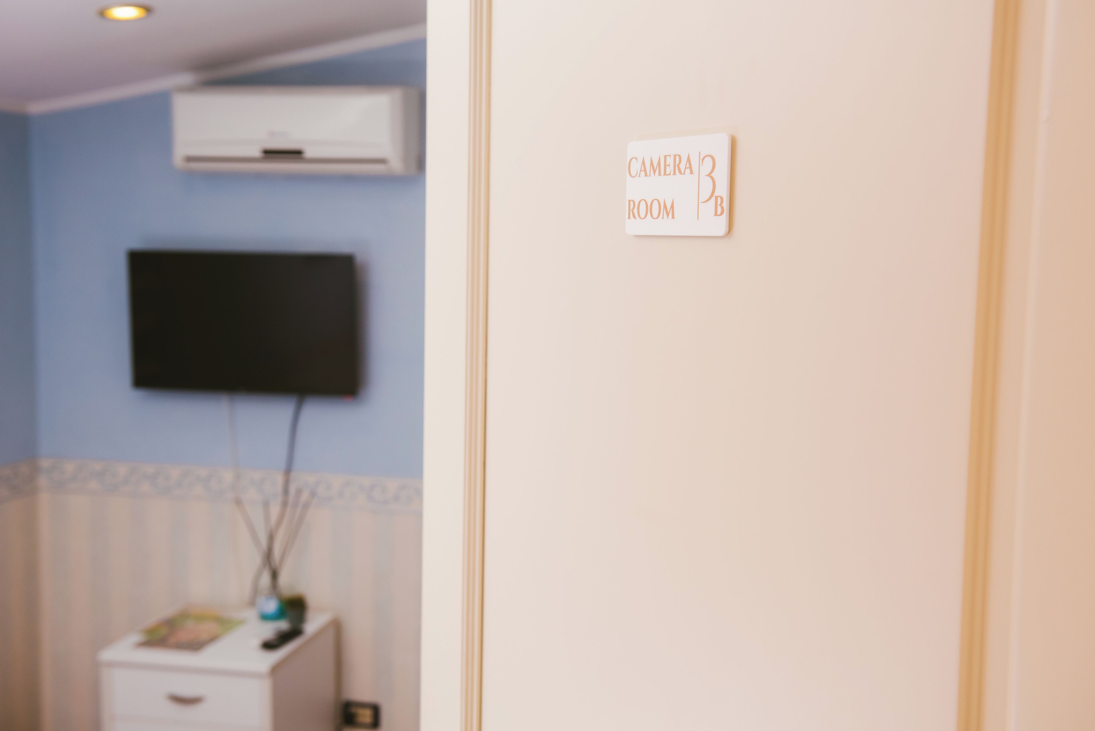 Ein Zimmer mit einem wandmontierten Flachbildfernseher, einer weißen Kommode mit einer Zeitschrift und einem Schild mit der Aufschrift 'Camera Room'.